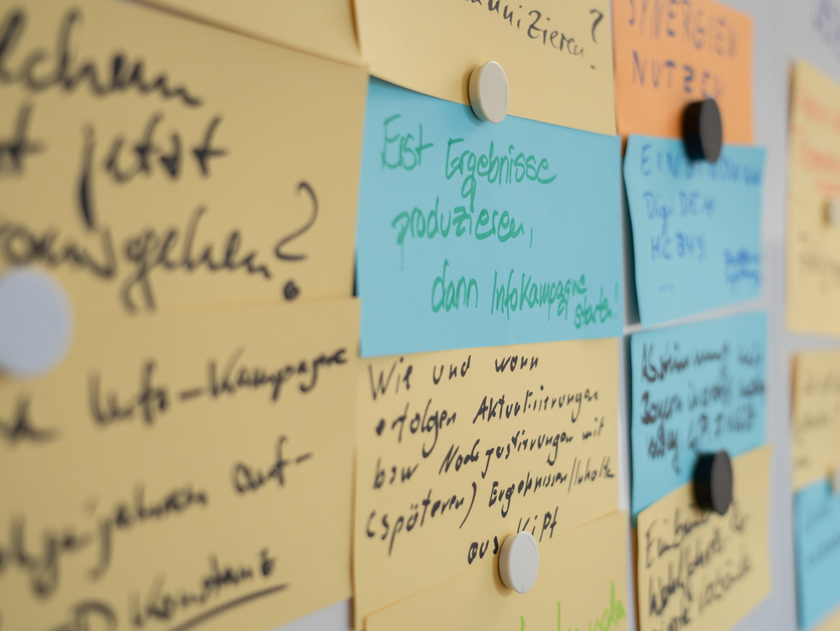 Verschiedenfarbige ausgefüllte Moderationskarten sind mit Magneten auf einem Whiteboard befestigt